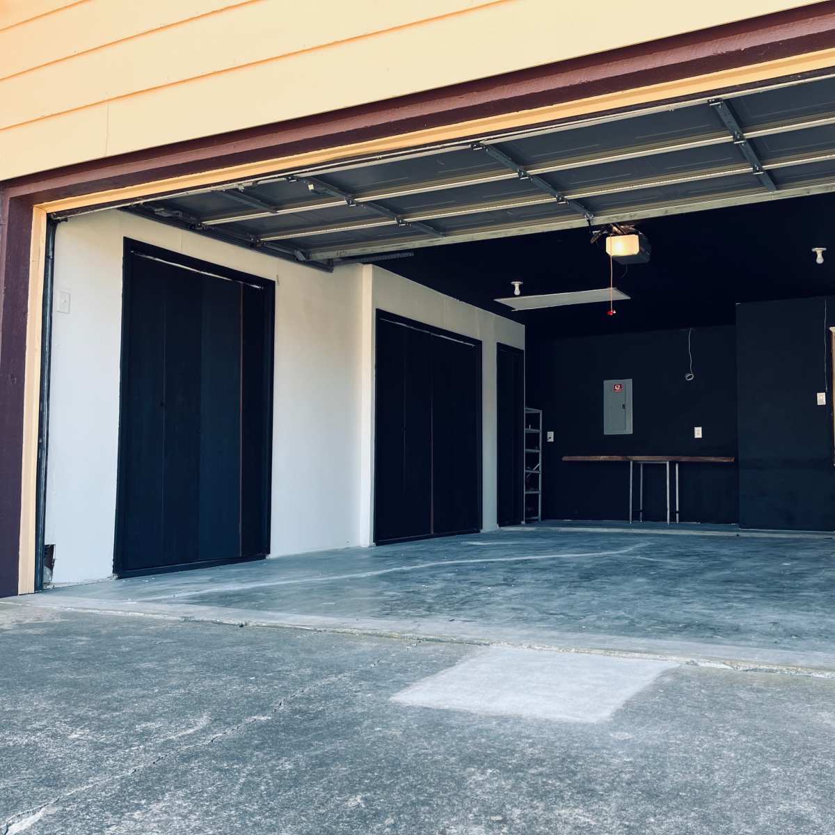 An empty garage with a concrete floor, black walls, and a near-complete ceiling installation, featuring a side door and a table against one wall.