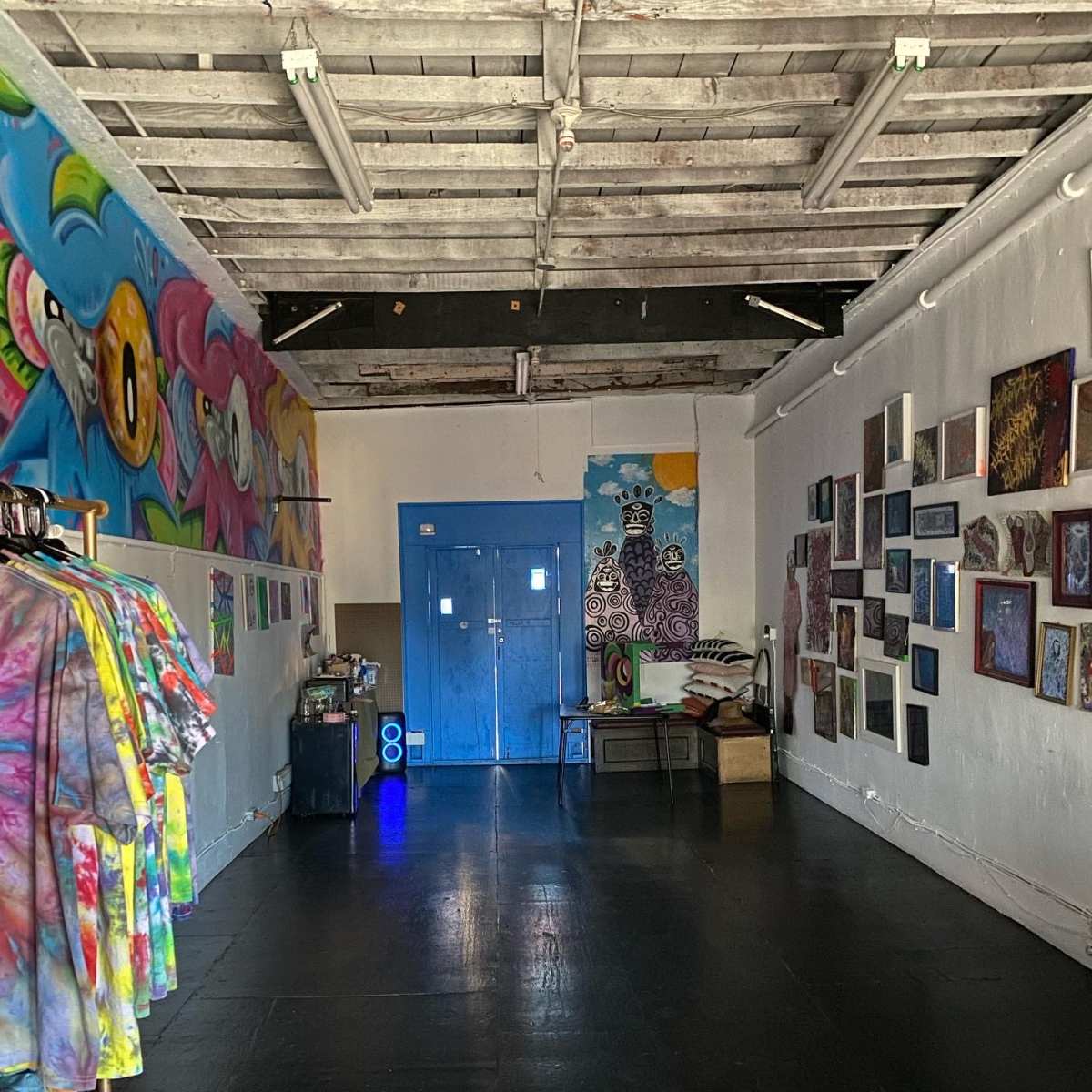 A spacious, brightly colored room with artistic murals on the walls, a blue door at the end, and clothing racks on one side.