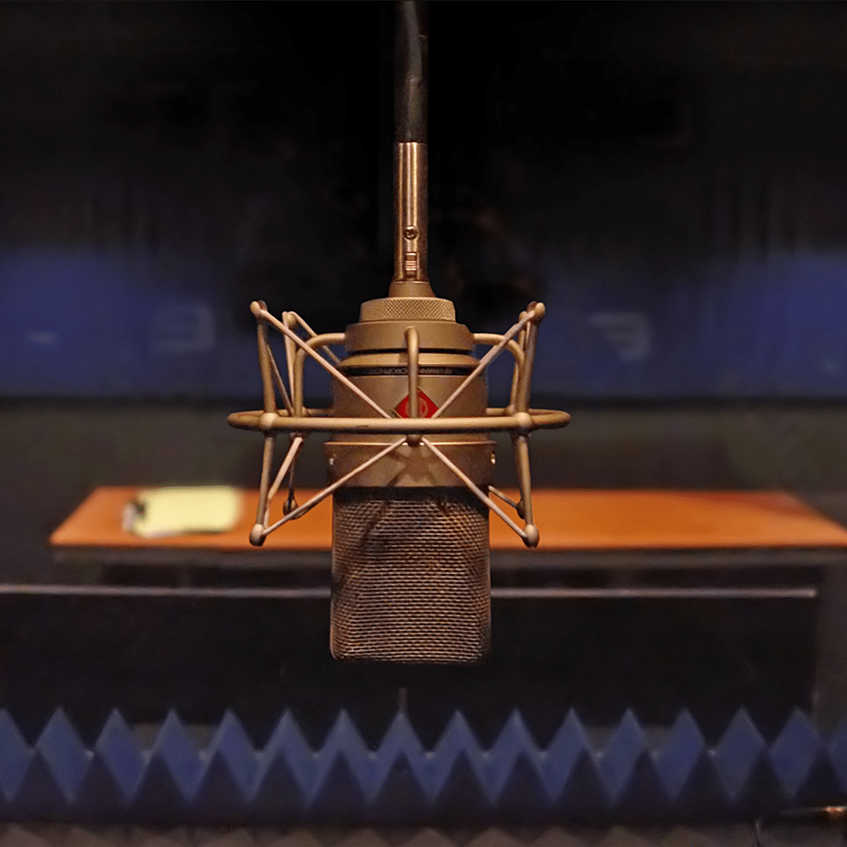 A vintage microphone is positioned in a soundproof recording studio with a wooden table in the background.