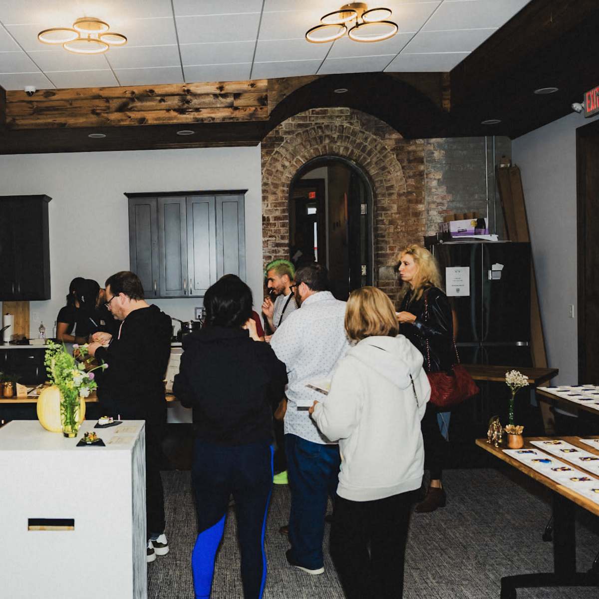 A group of people are gathered in a spacious room with dark wood accents, engaging in conversation and sampling food at a modern event.