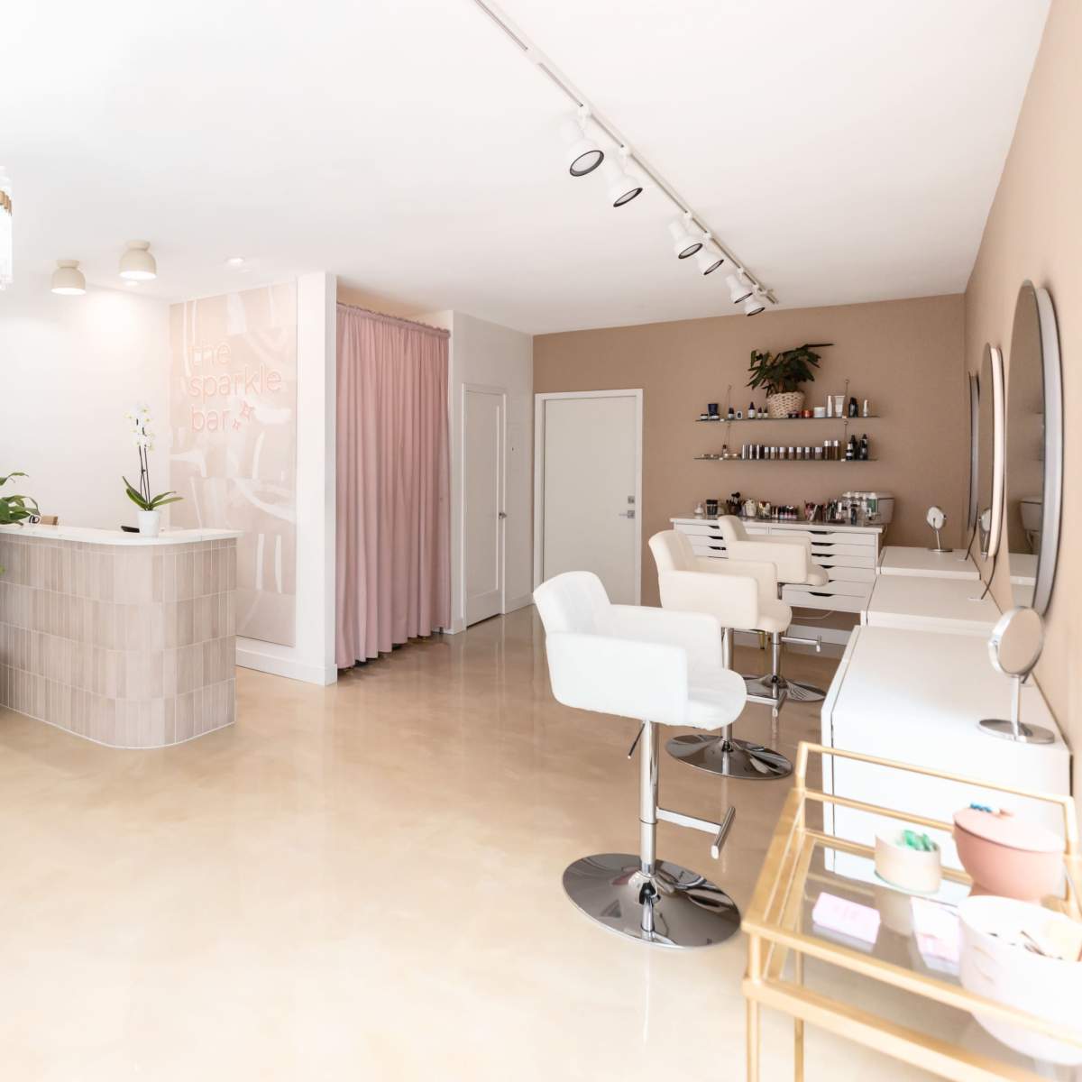 A modern beauty salon interior featuring a reception desk, styling stations, and decorative elements in neutral tones.