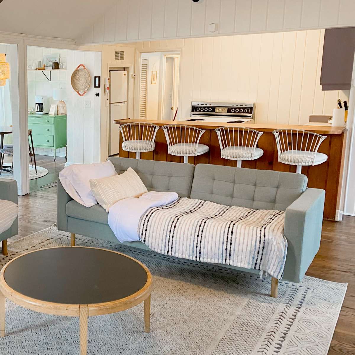 A cozy living room featuring two light-colored sofas flanking a round coffee table, with a view into a kitchen area and dining space.