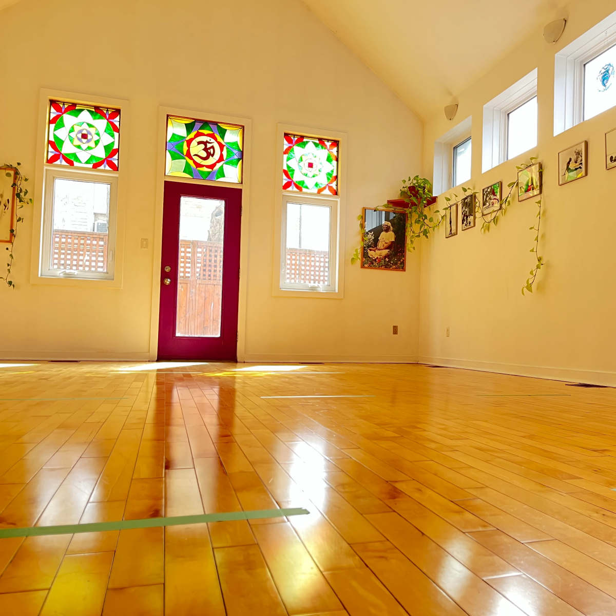 A spacious, well-lit room with wooden flooring, colorful stained glass windows, and framed images on the walls.