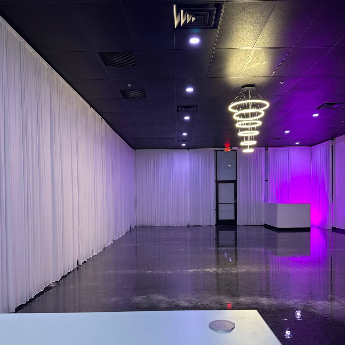 A spacious interior room with white drapes along the walls, polished floors, and modern lighting fixtures.
