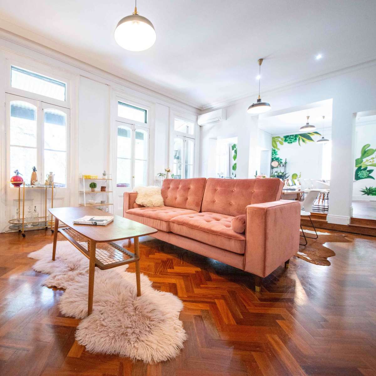 The living room features a pink sofa, a wooden coffee table, and a decorative fur rug, with large windows allowing natural light to fill the space.