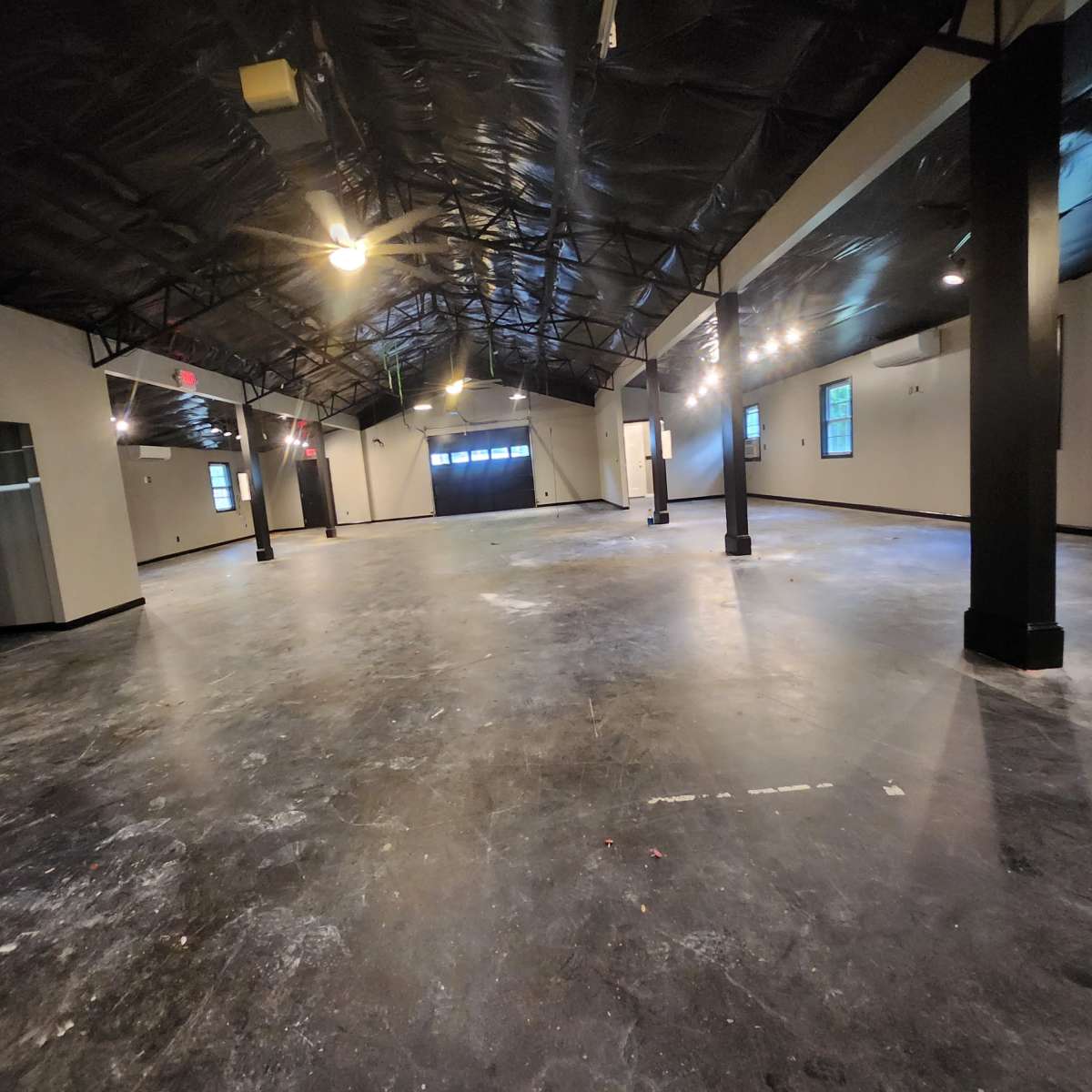 A large, empty indoor space with a polished concrete floor, exposed beams, and several overhead lights.