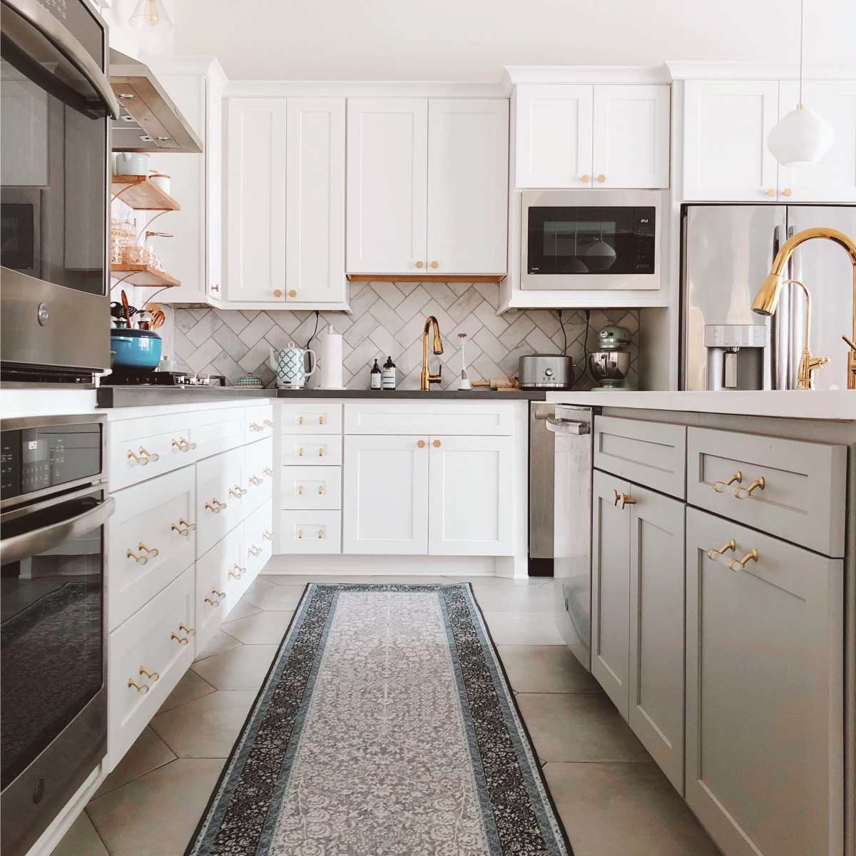 A modern kitchen features white cabinetry, stainless steel appliances, and a long decorative rug extending down the center.