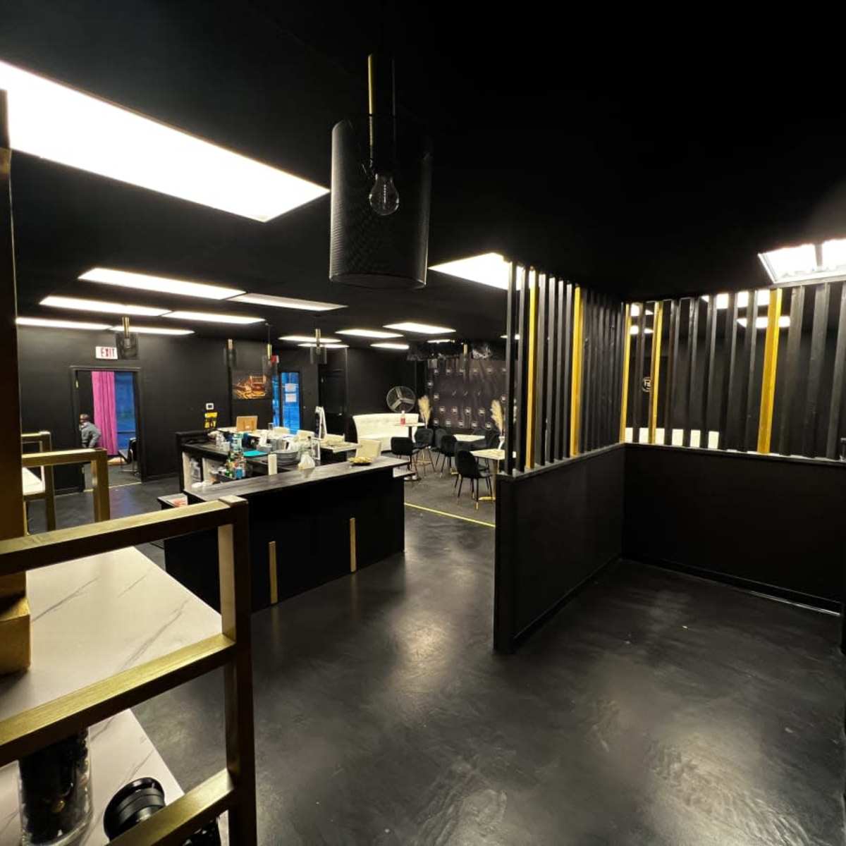 An interior space featuring black walls, a polished floor, and contrasting gold accents, with various furniture arranged for a modern, minimalist design.