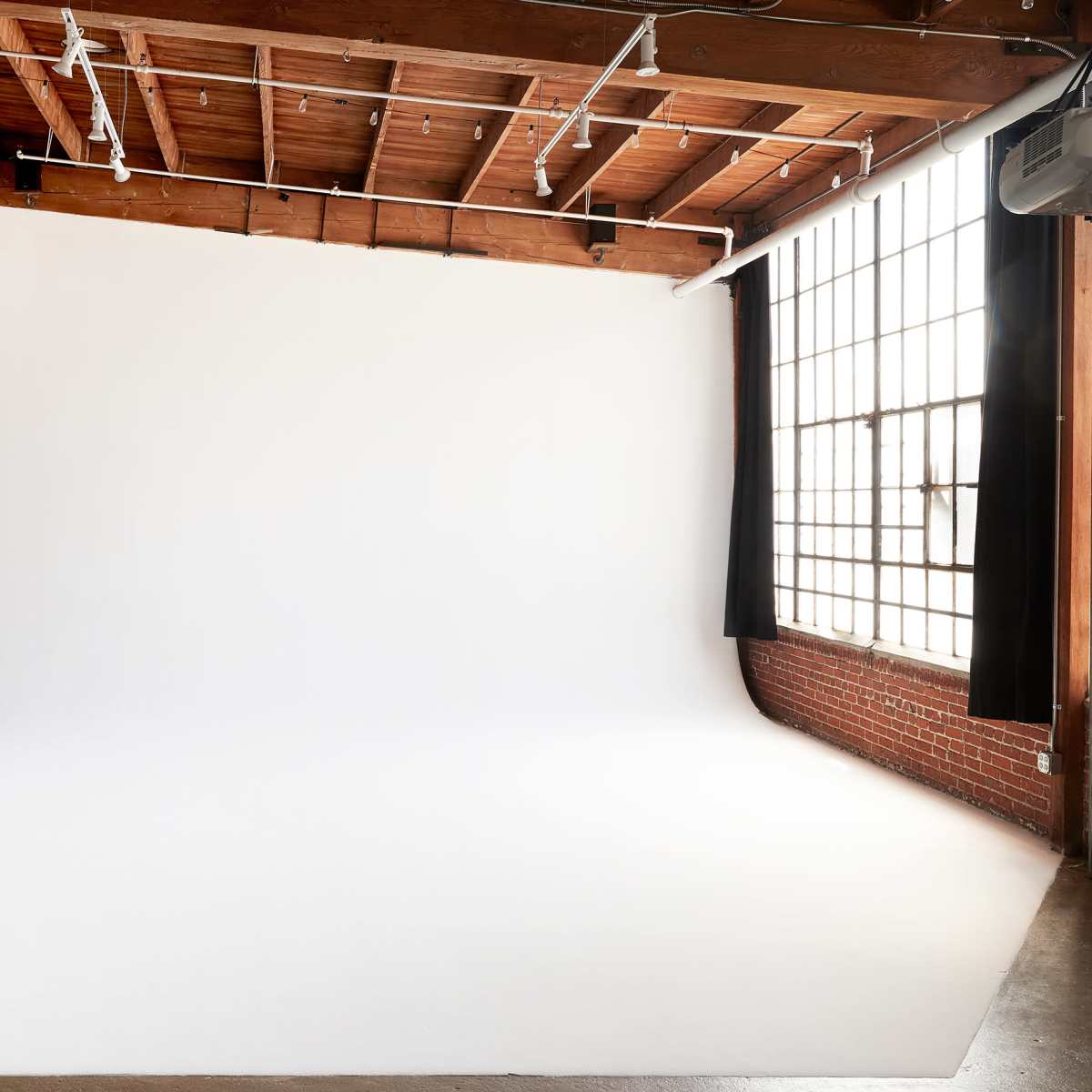 A spacious photography studio featuring a white seamless backdrop, large windows, and exposed wooden beams.