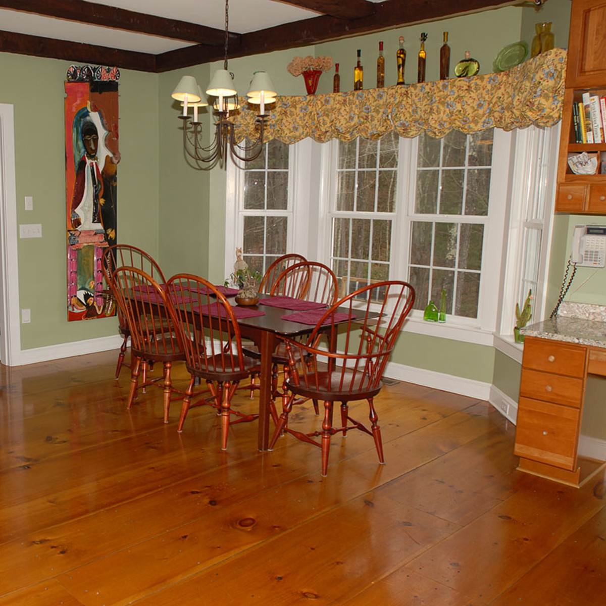 A dining area features a wooden table surrounded by chairs, with large windows and a doorway leading to another room.