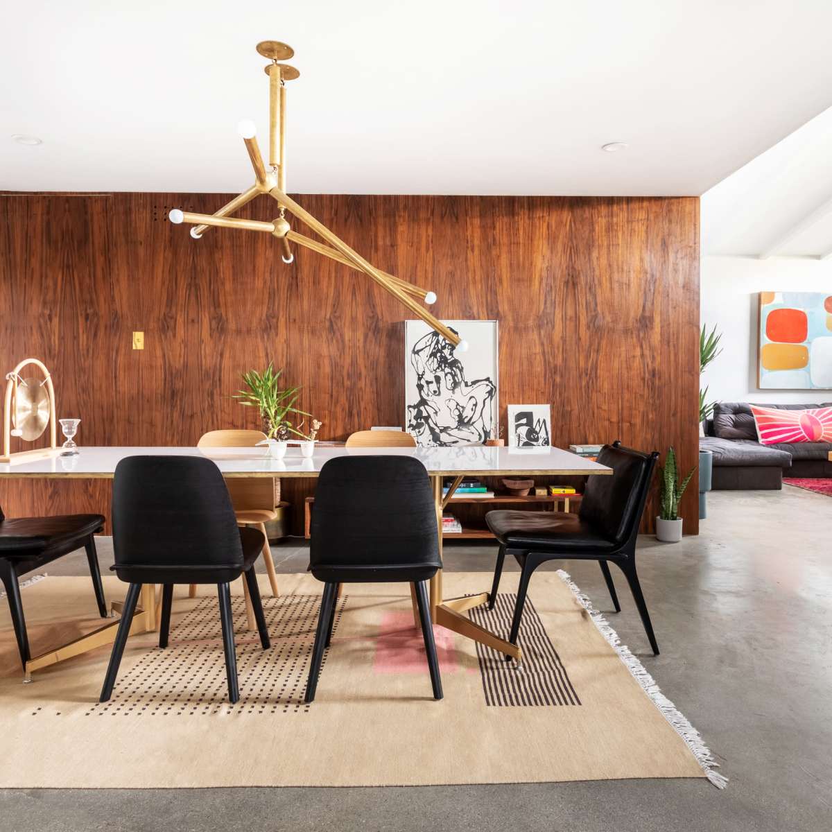 A dining area features a large table surrounded by black chairs, with wooden wall paneling and modern artwork in the background.
