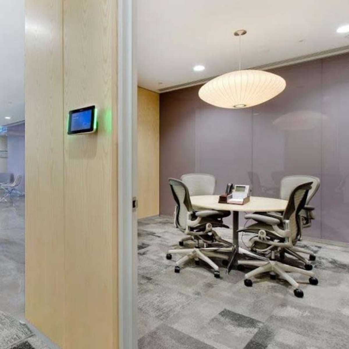 A modern office space with a reception area on the left and a small meeting room with round tables and chairs on the right.