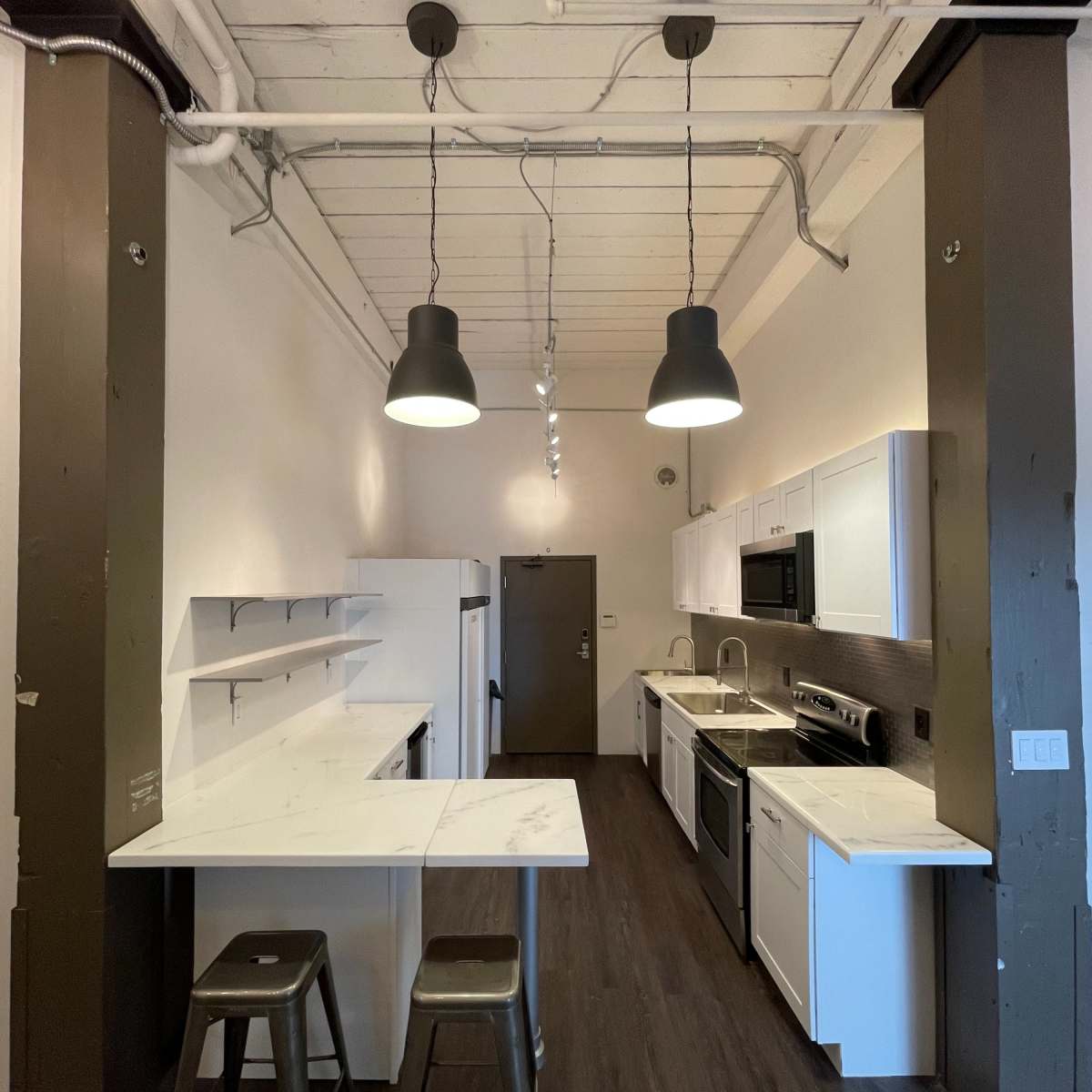 A modern kitchen with white cabinets, stainless steel appliances, and two metal stools situated at a small breakfast bar.