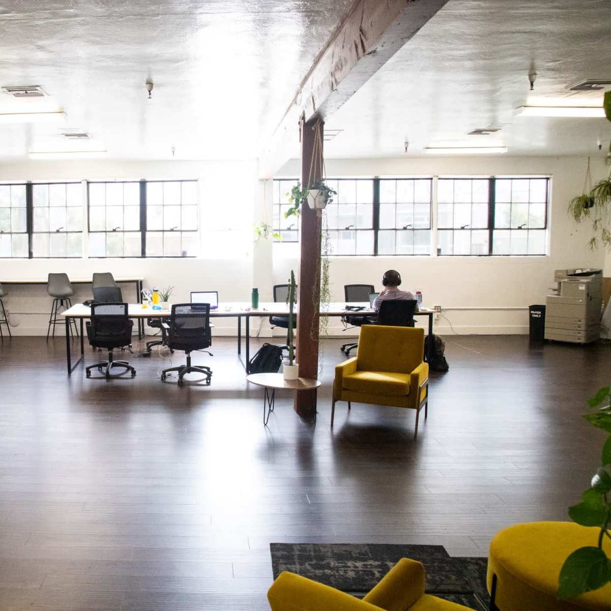 A spacious office interior with desks, chairs, and large windows allowing natural light.