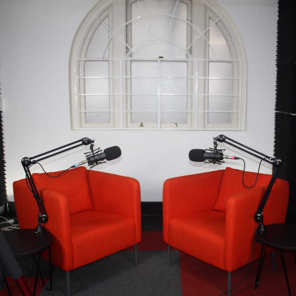 Two orange chairs positioned in front of a window in a studio setup, equipped with microphone stands and small side tables.