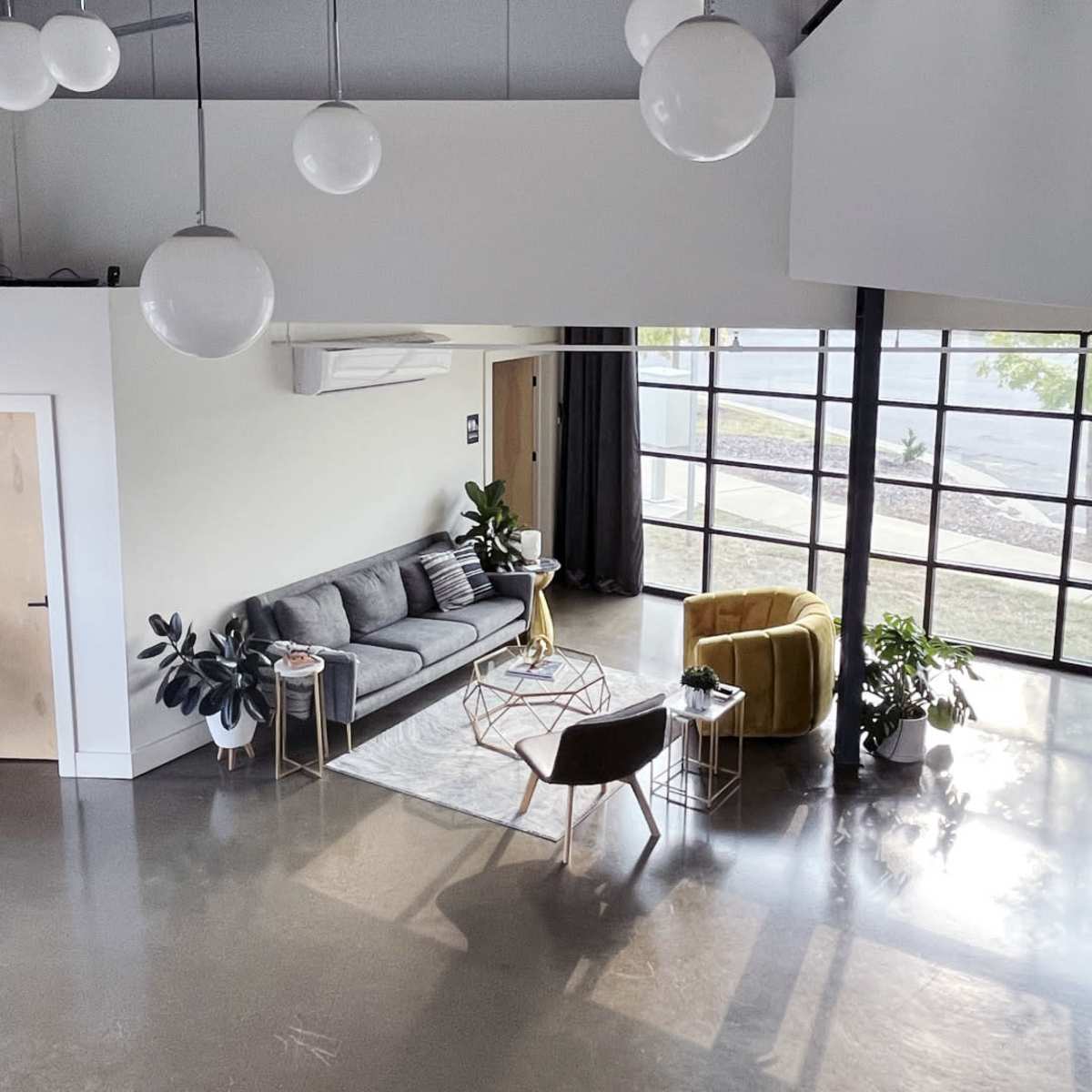 The interior features a modern lounge area with a gray sofa, a yellow armchair, and large windows allowing natural light to fill the space.