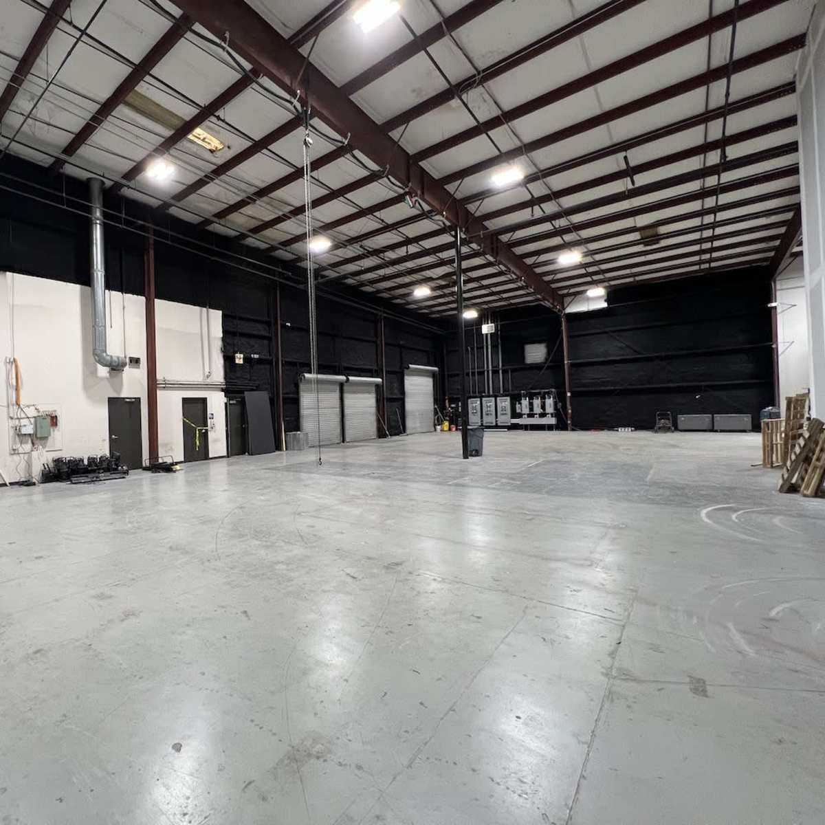A spacious industrial warehouse with high ceilings, concrete floors, and various electrical panels along the walls.