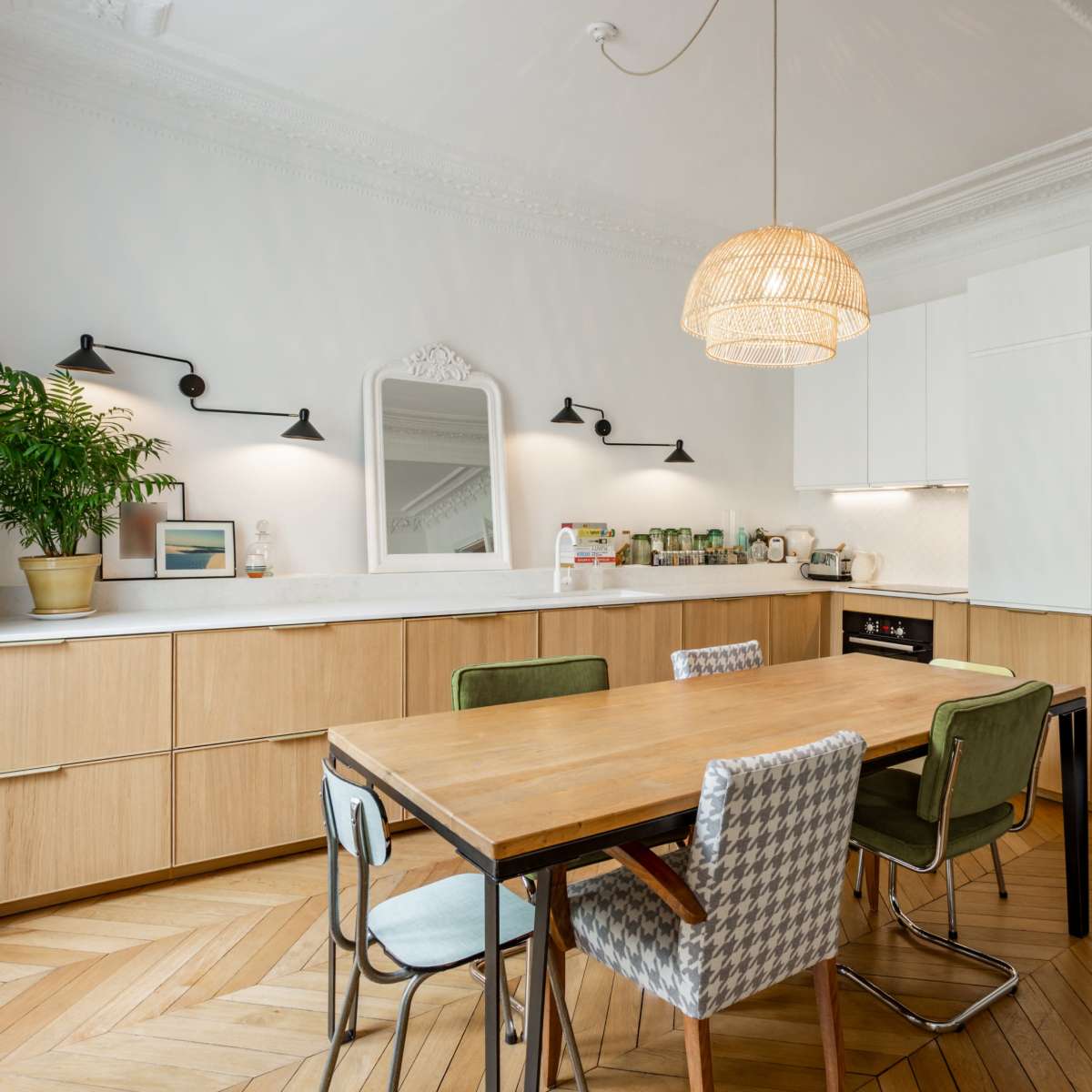 A modern kitchen features wooden cabinetry, a large dining table with chairs, and a woven pendant light.