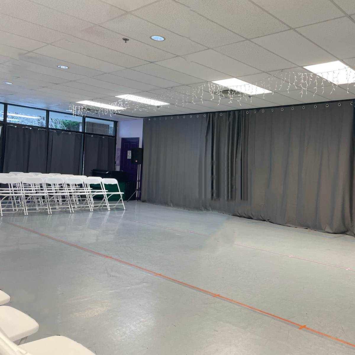 A spacious room with gray curtains, white folding chairs arranged in rows, and a smooth gray floor.