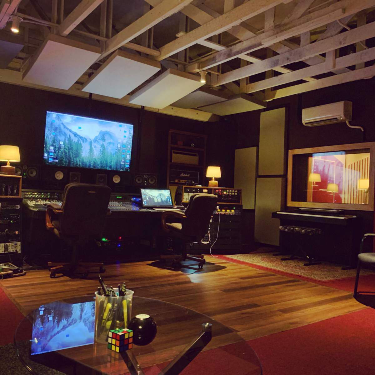 A music studio is equipped with a central mixing desk, monitors, and a variety of audio equipment, surrounded by seating and decorative lighting.