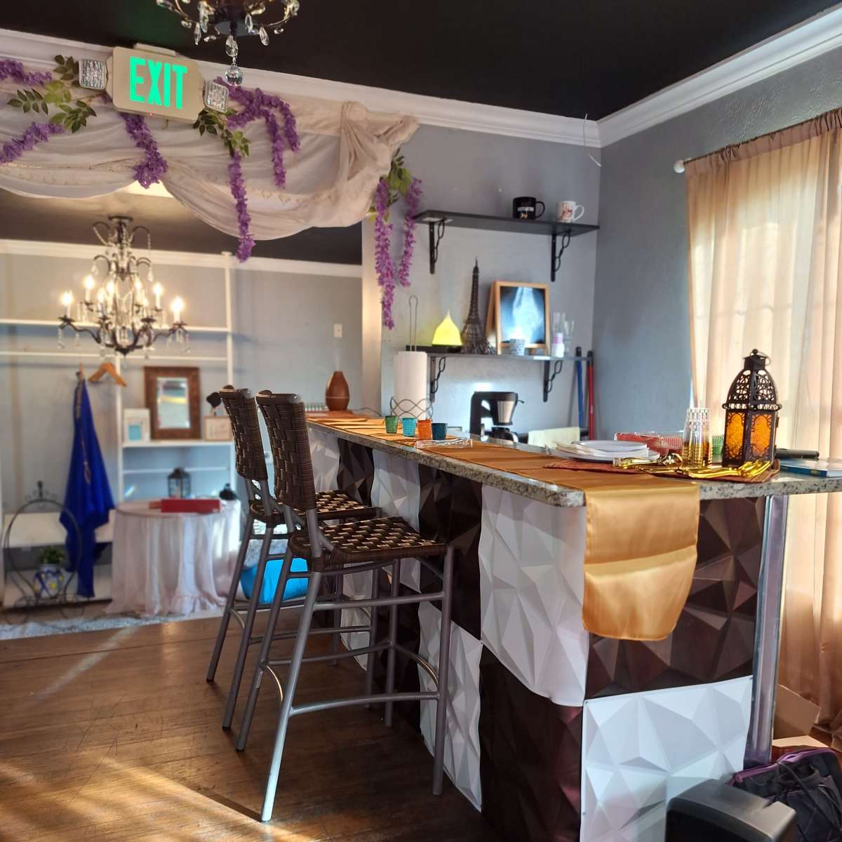 A modern bar area with a geometric-patterned countertop and high stools, decorated with hanging grapevines and a chandelier.