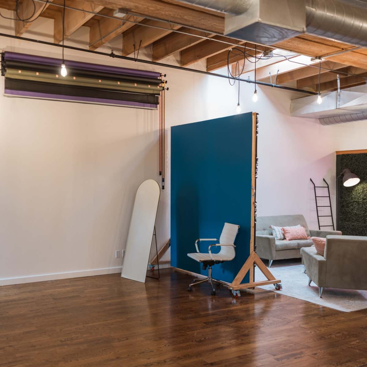 A spacious, well-lit interior with wooden flooring, featuring a blue backdrop, a chair on wheels, a mirror, and soft seating areas.