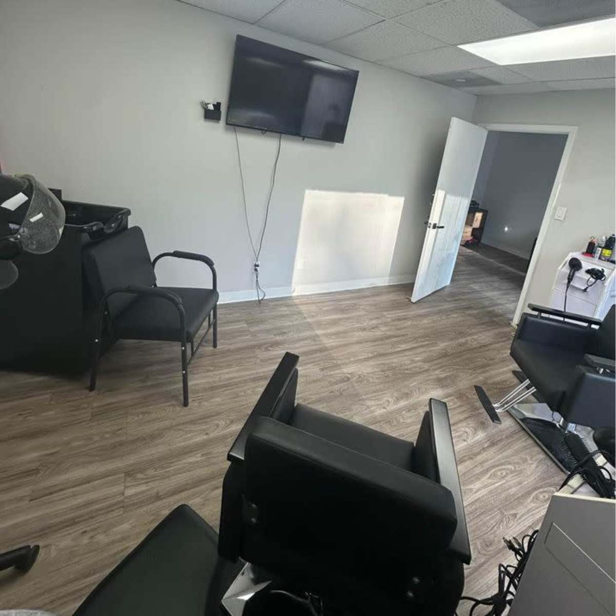 A barbershop interior with two black chairs, a wall-mounted television, and a door leading to another room.