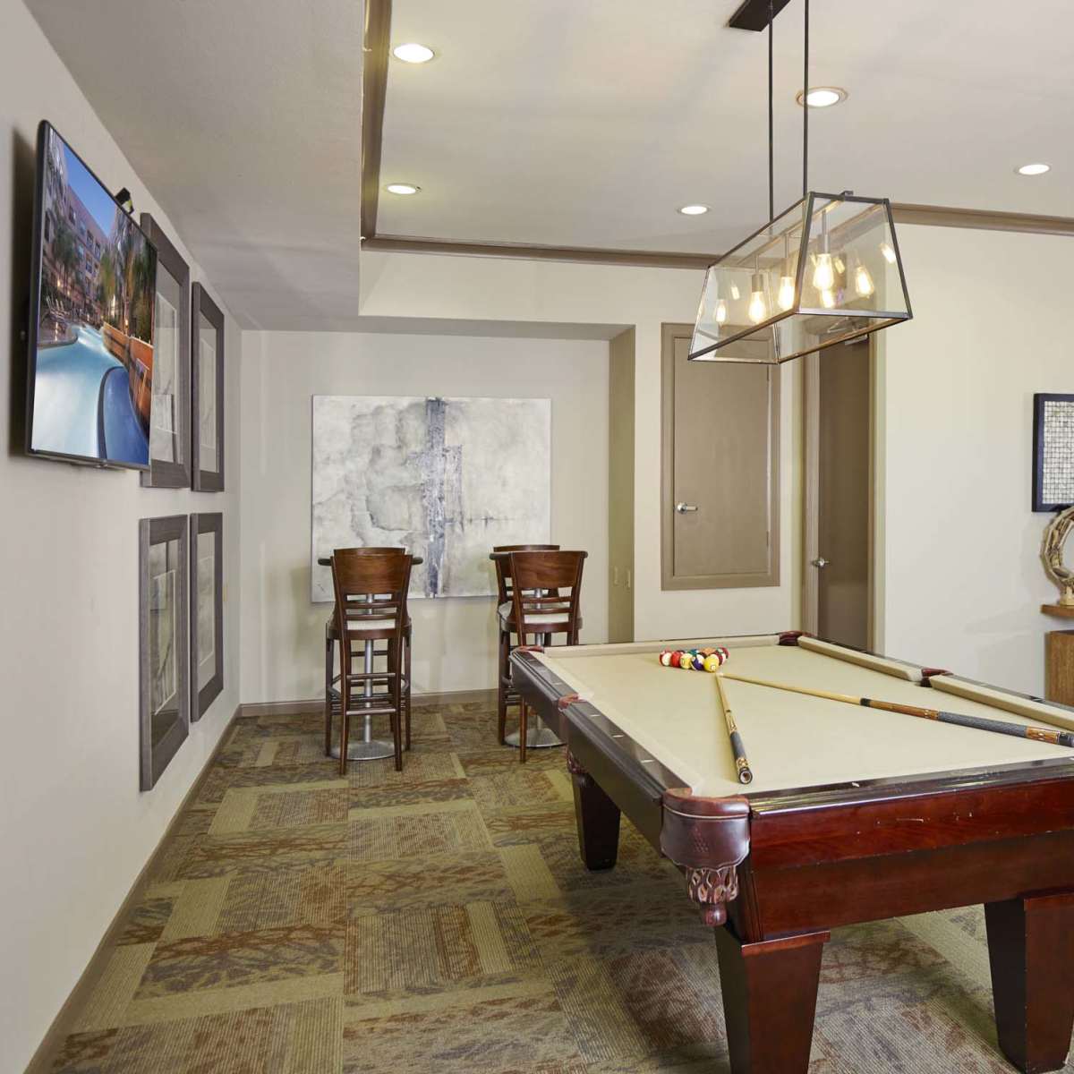 A recreational room with a billiards table, two bar stools, wall art, and a seating area.