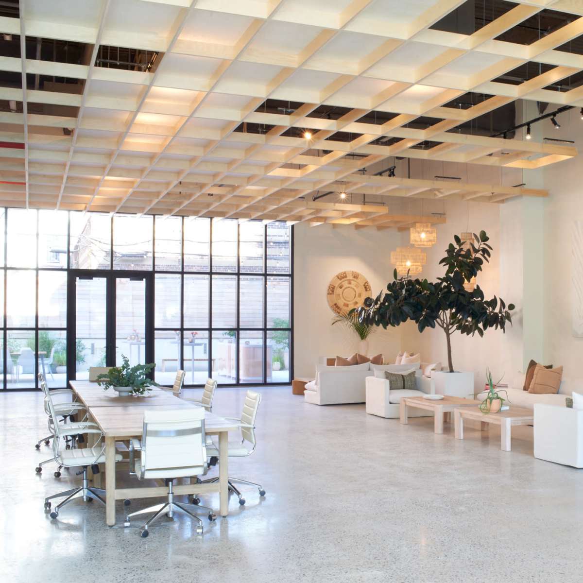 A spacious, modern interior featuring a large seating area with white furniture, a wooden ceiling grid, and decorative plants.