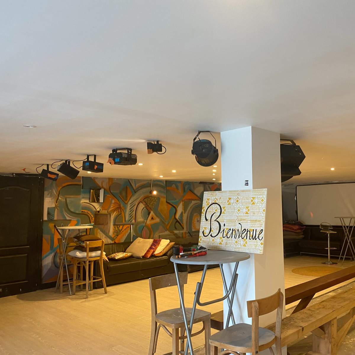A spacious, brightly lit indoor venue with a bar area, seating, and decorative murals on the walls.