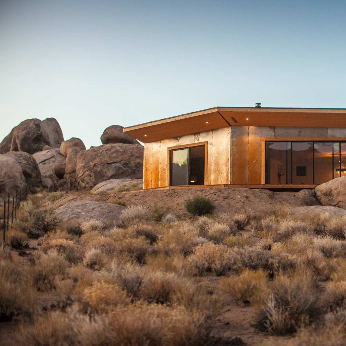 A modern house with large windows is situated among rocky terrain and sparse vegetation.