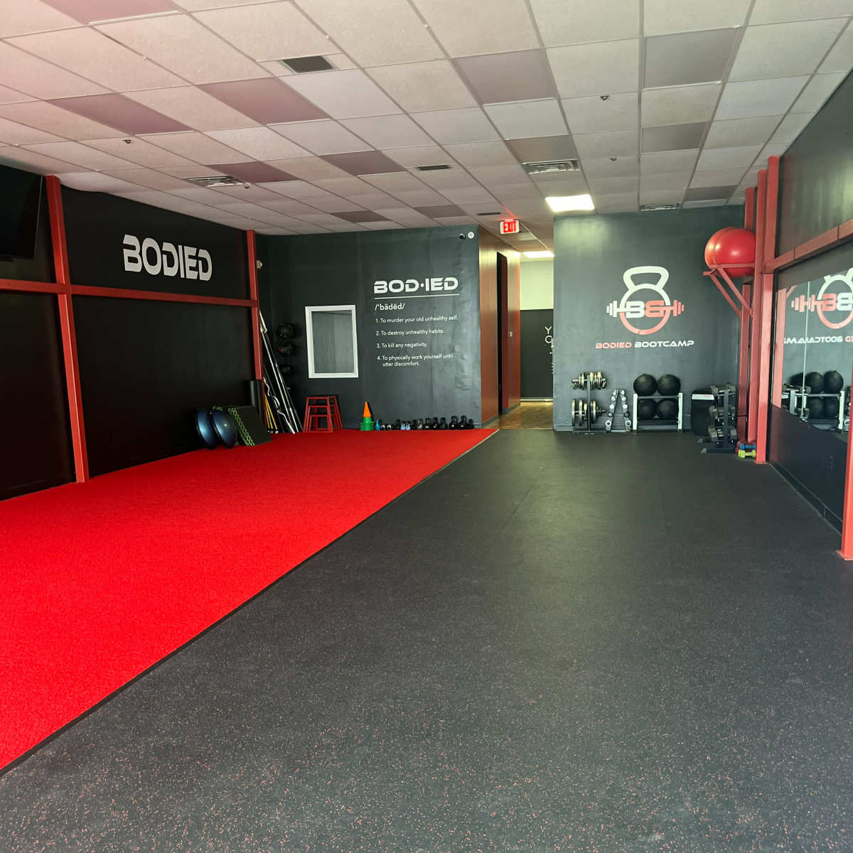 A fitness studio with black walls, red flooring, and various exercise equipment along the sides.