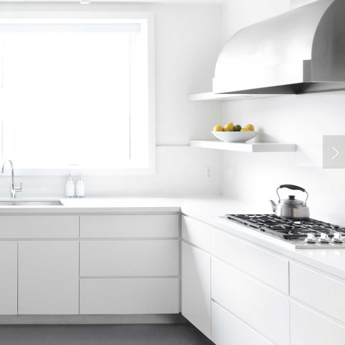 A modern kitchen features white cabinetry, a large window, stainless steel appliances, and a sleek countertop.