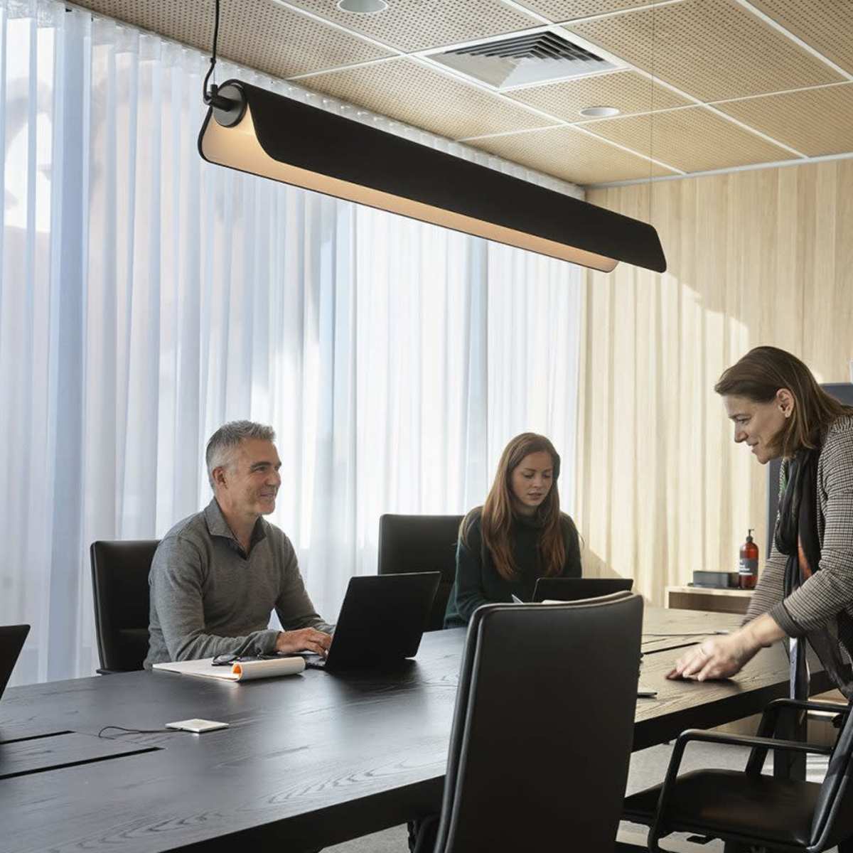 A group of four professionals is seated around a conference table in a well-lit meeting room, with one person standing and arranging materials.
