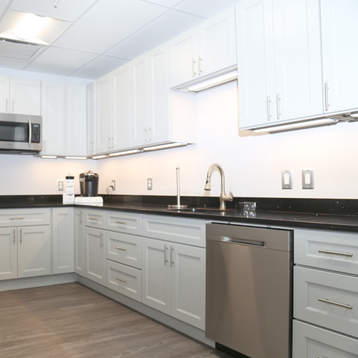A modern kitchen with gray cabinets, stainless steel appliances, and a dark countertop.
