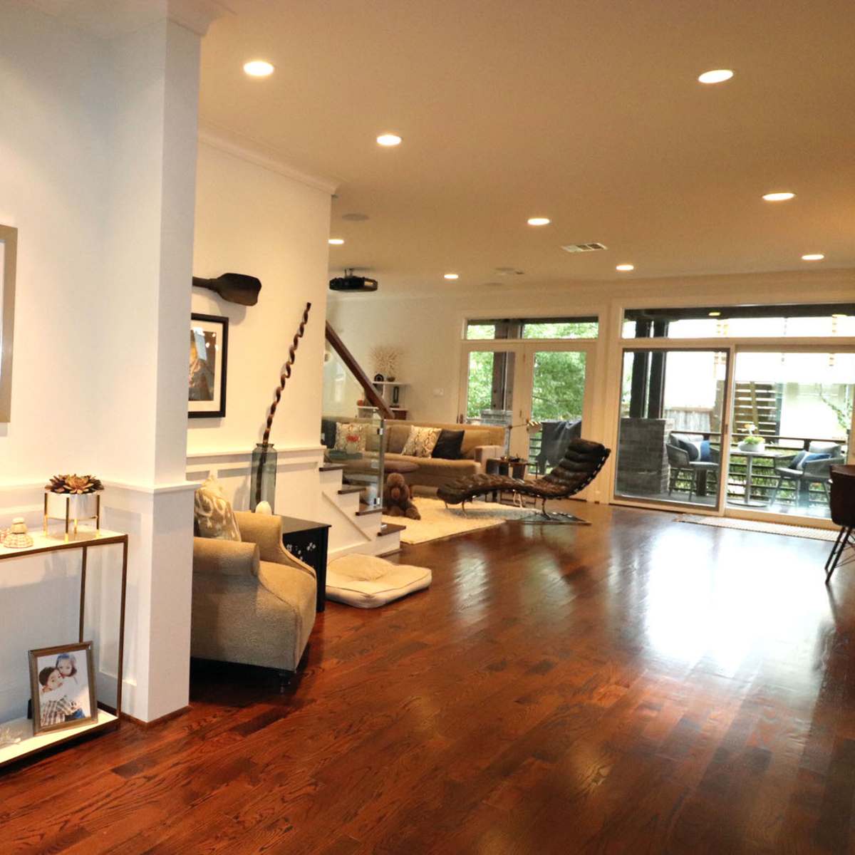 A spacious living area with wooden flooring, modern furniture, and large windows that open to a patio.