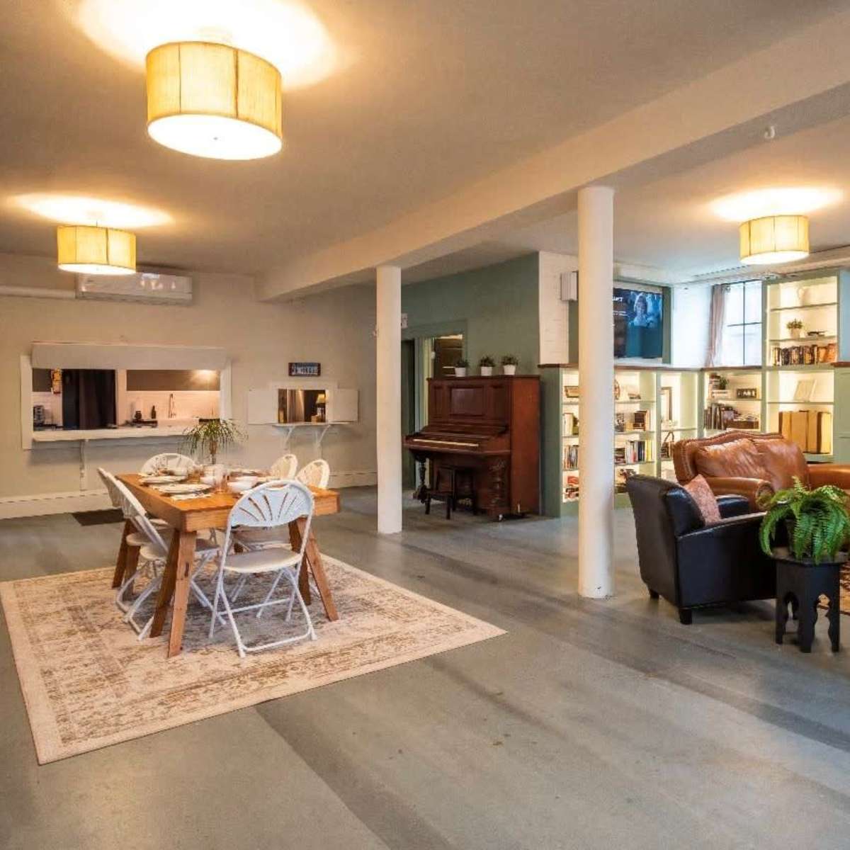 A spacious room featuring a dining area with a table and chairs, a living area with a sofa and armchairs, a piano, and a fireplace, along with decorative shelves and light fixtures.