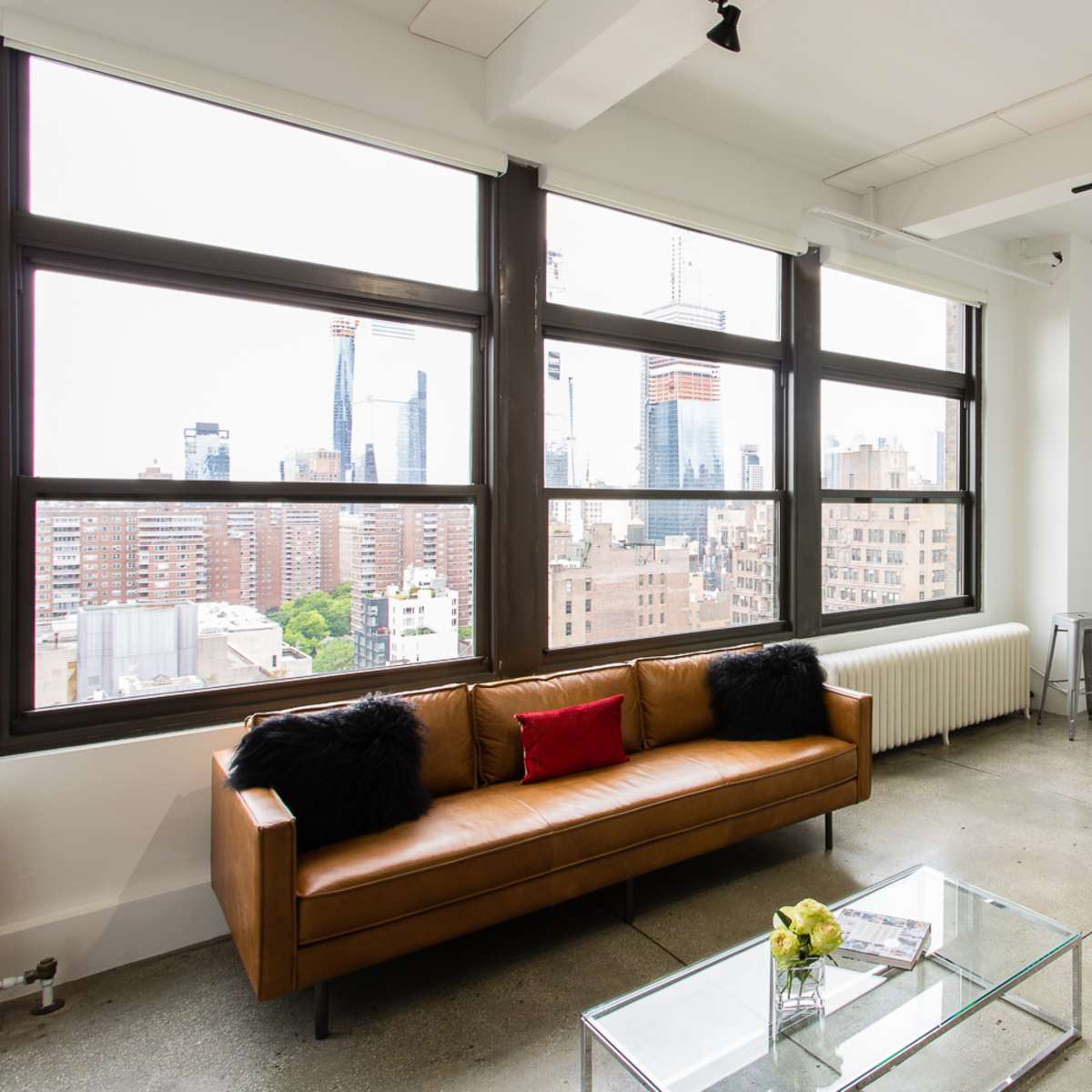 A modern living space features a brown leather sofa, a green patterned chair, and a glass coffee table with a view of the city through large windows.
