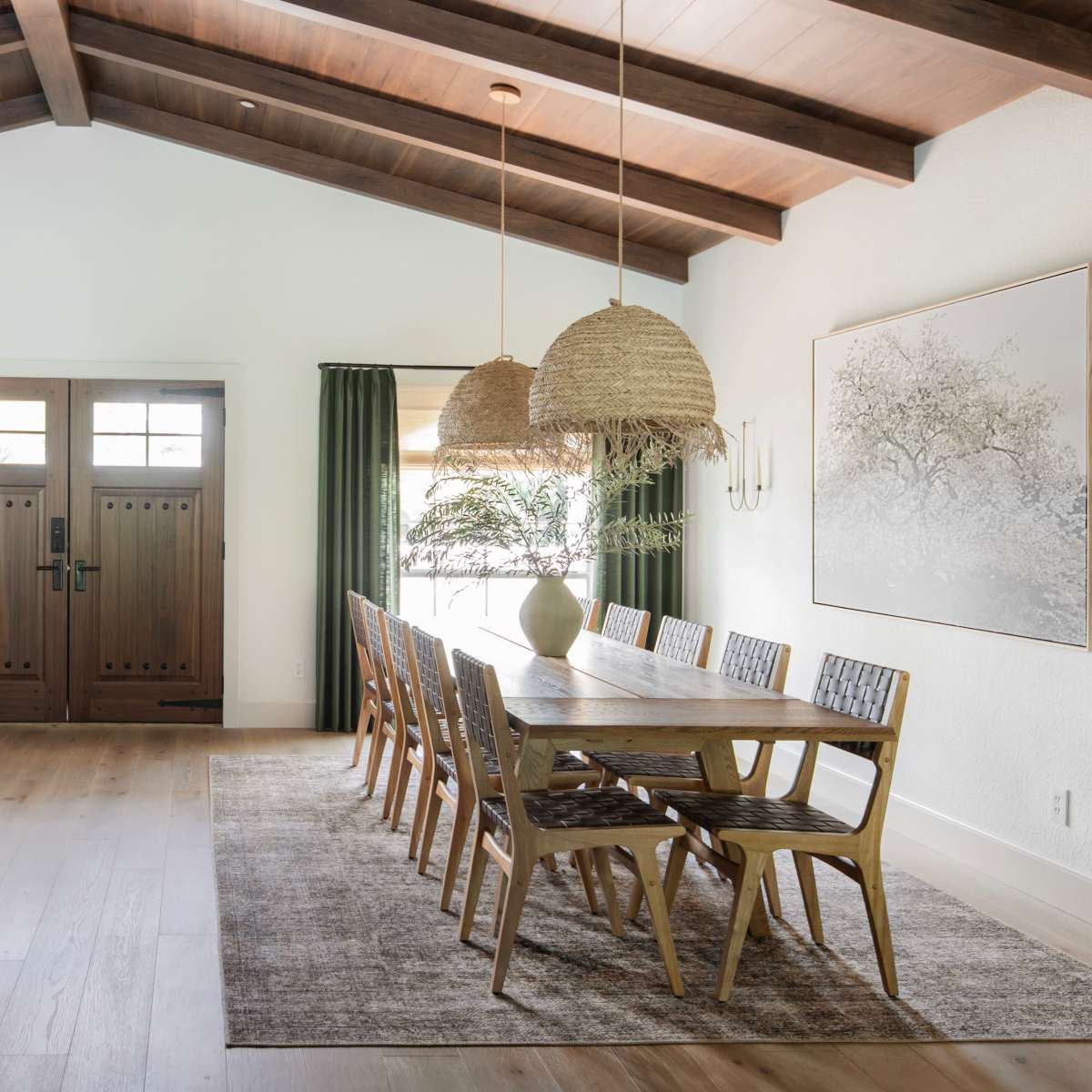 A spacious dining area features a long wooden table surrounded by chairs, with large pendant lights overhead and a decorative mirror on the wall.
