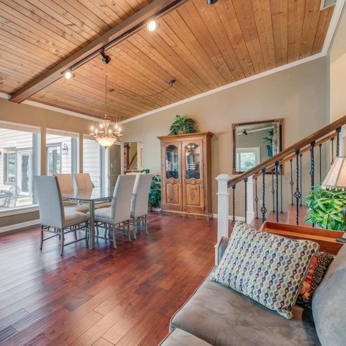 A spacious living and dining area with wooden flooring, a wooden ceiling, and large windows that provide a view of the outdoors.