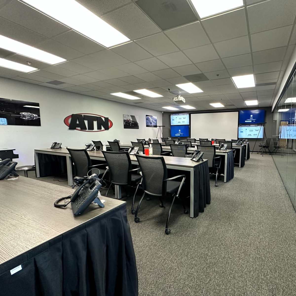 A modern conference room is set up with rows of tables and chairs, equipped with phones and screens displaying information.