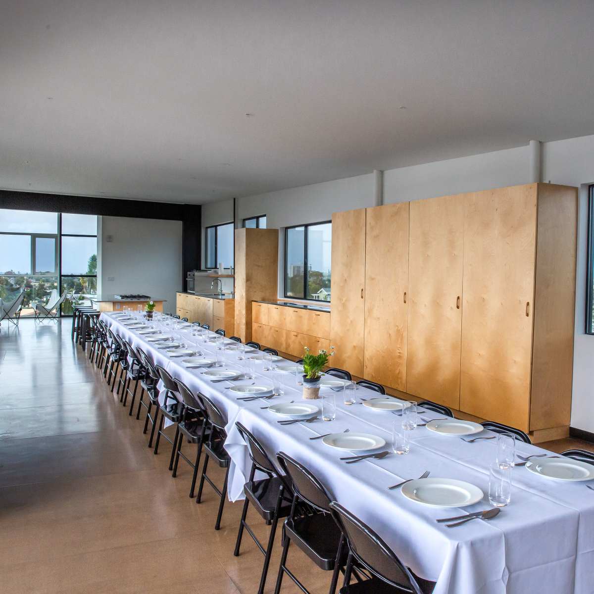 A long dining table set for a meal is arranged in a bright, modern room with large windows.