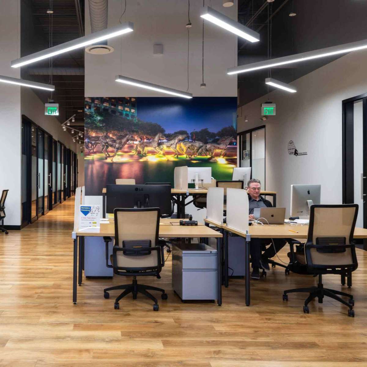 A modern office space with several workstations, featuring wooden floors and a large mural of a cityscape on the wall.