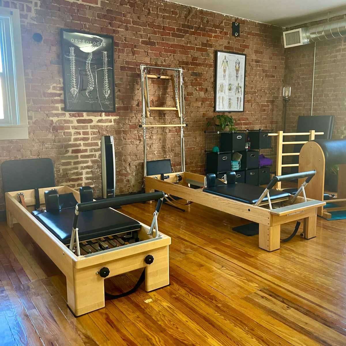 A Pilates studio with wooden equipment, exposed brick walls, and large windows allowing natural light to enter.