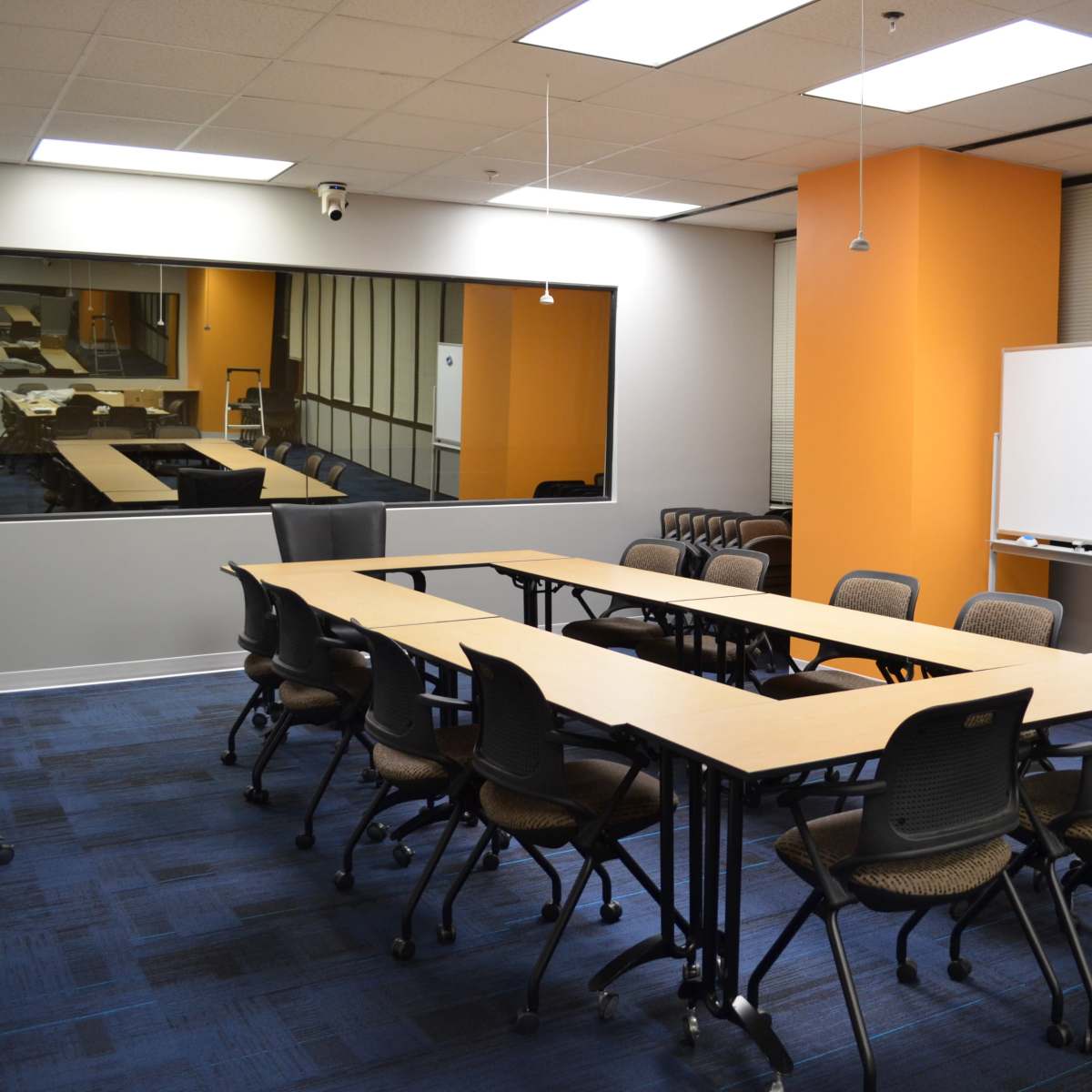 A conference room with a rectangular table surrounded by chairs, a whiteboard, and large windows.