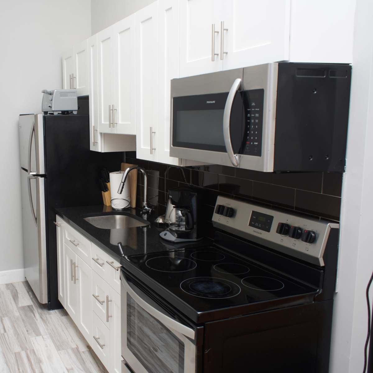 A modern kitchen featuring white cabinets, stainless steel appliances, and a black countertop.