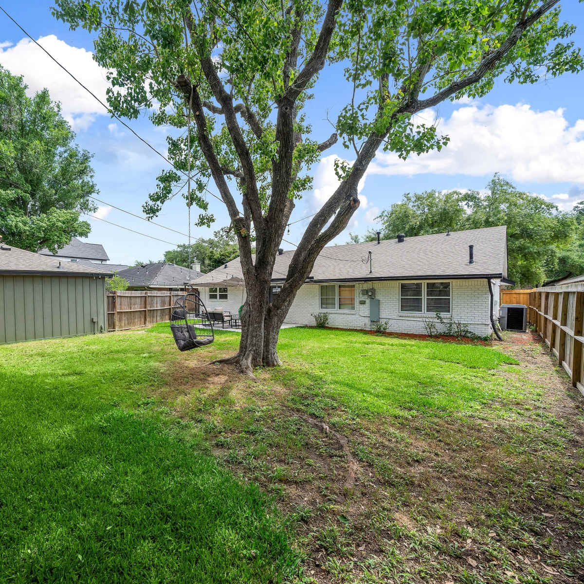 A spacious backyard with a tree, a swing, and a fence surrounding the property, along with a nearby shed.