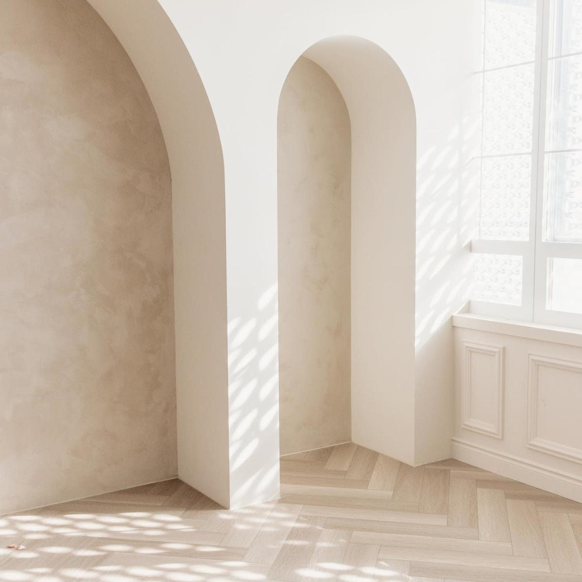 A minimalist interior with arched walls and soft natural light streaming in through a window.