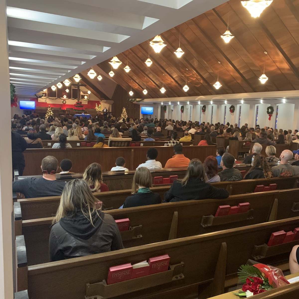 A large congregation is gathered in a church, filling the pews during a service decorated for the holiday season.