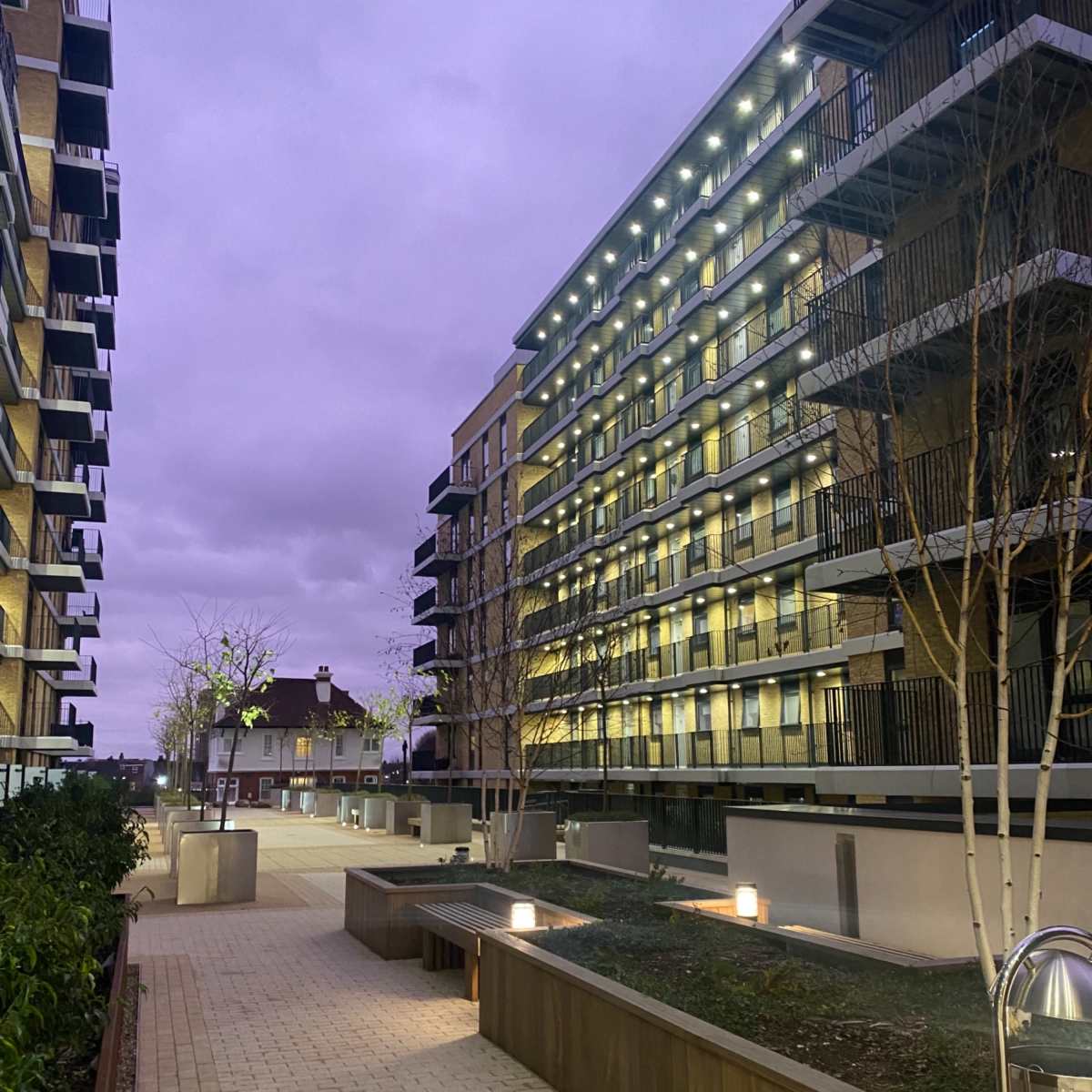 A modern residential pathway flanked by two buildings with balconies, under a twilight sky.